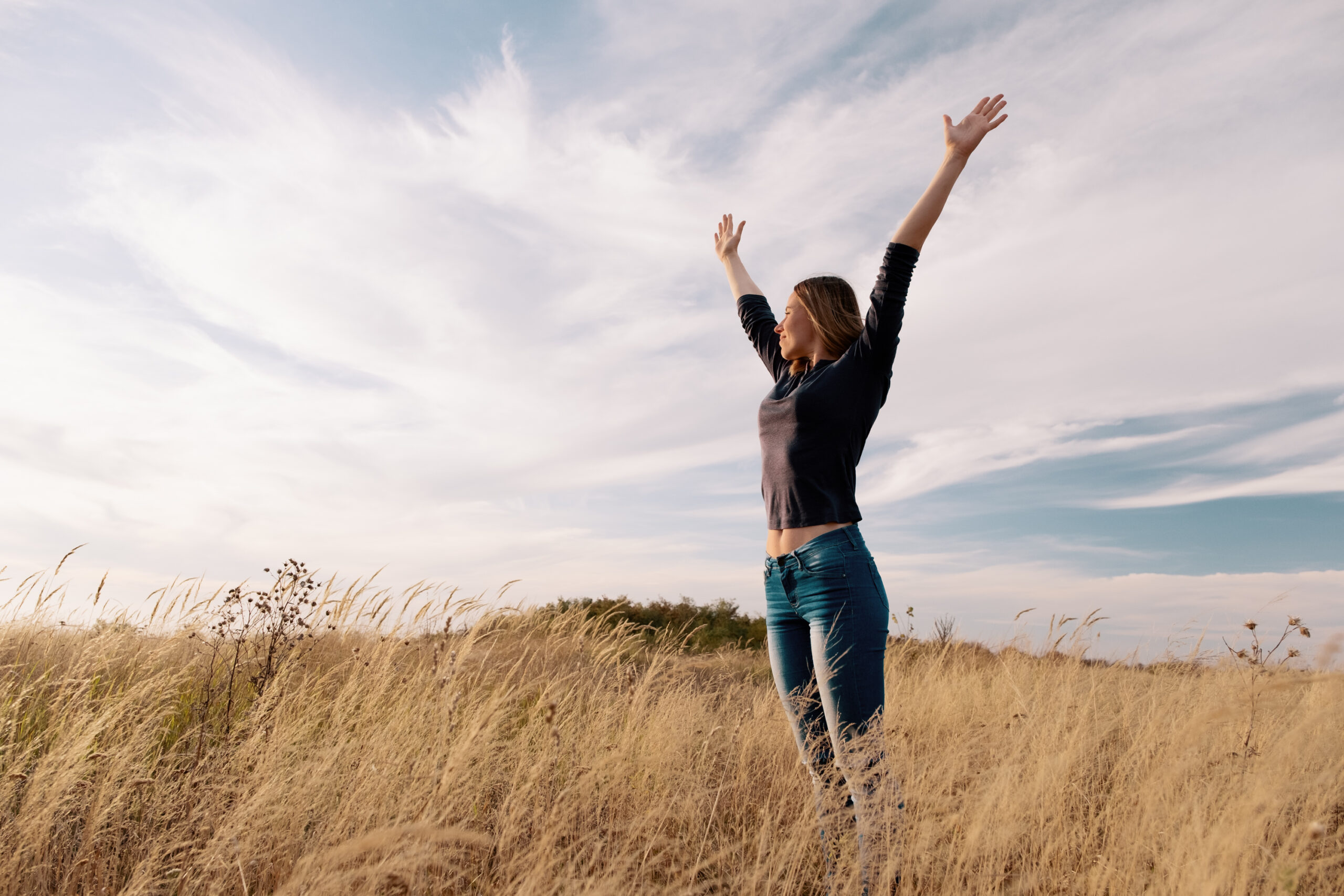 Young woman enjoying nature and freedom in a golden field under the blue sky